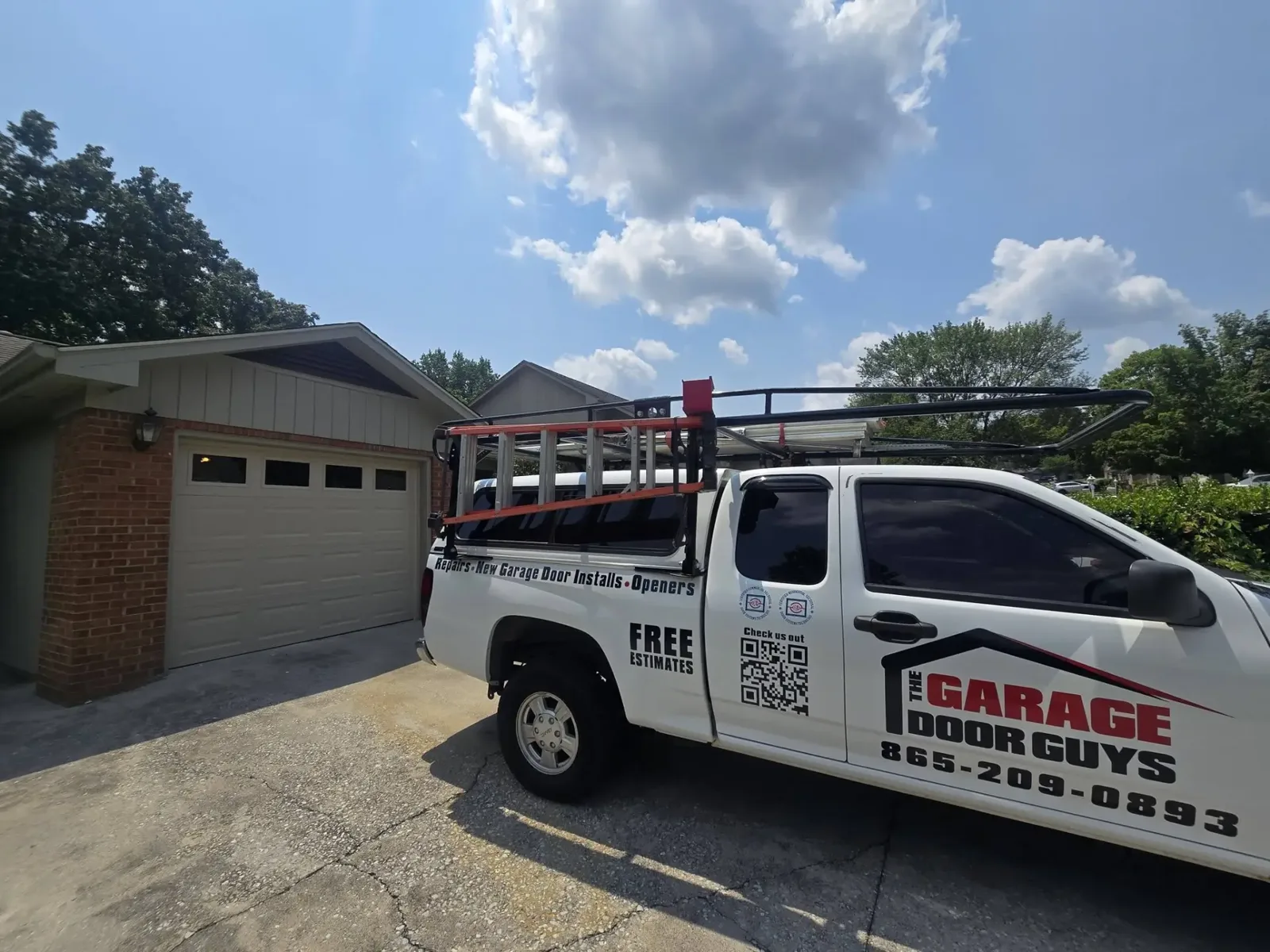 The Garage Door Guys truck in a driveway in front of a tan house with a beige garage door