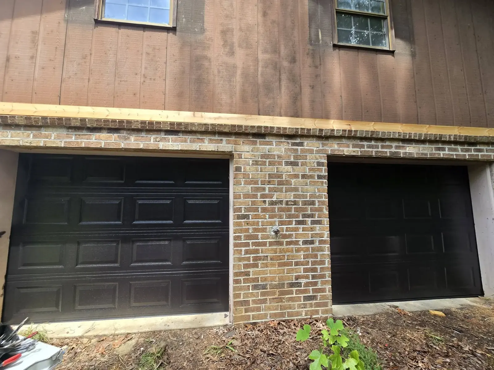 Two matching black single garage doors installed on a brick and wood home