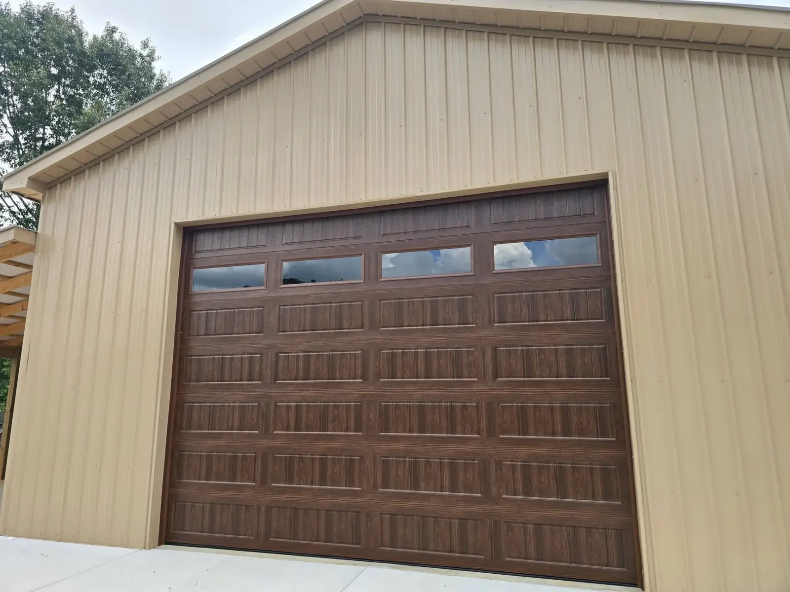 Walnut wood-look insulated garage door installed on a tan metal barn