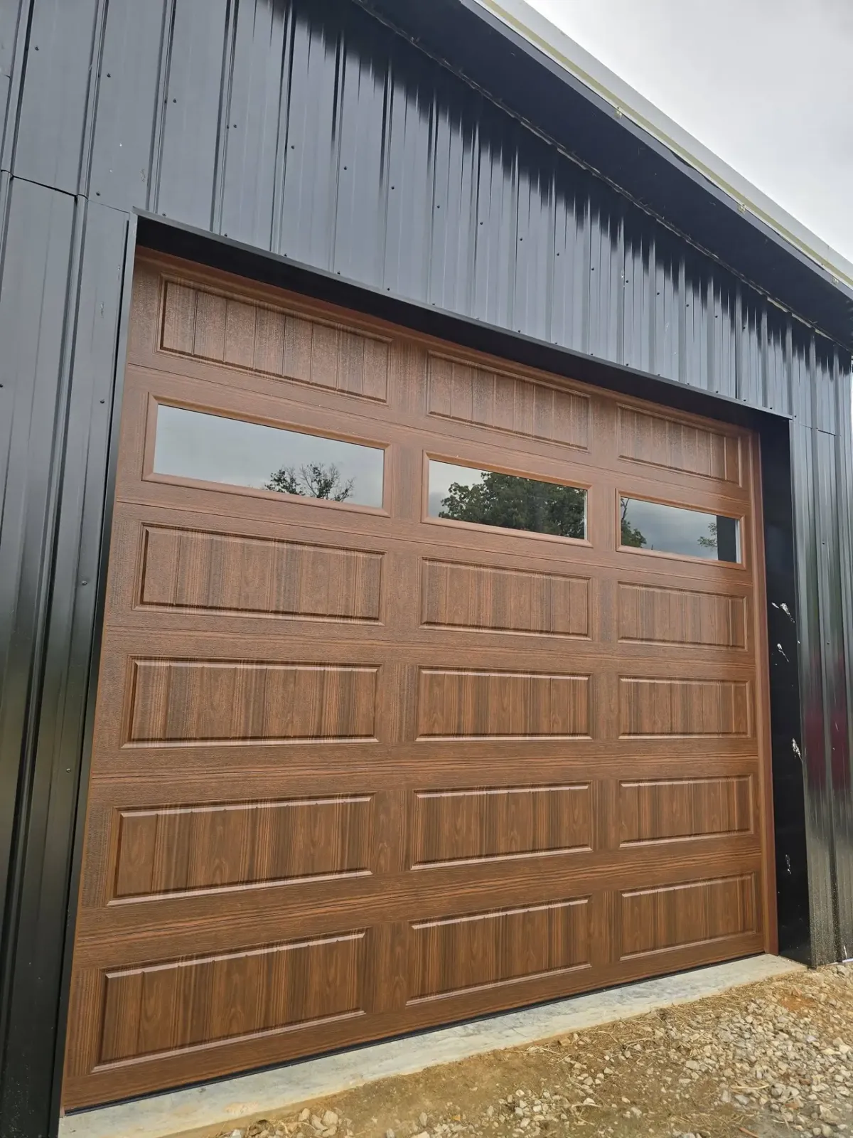 Wood-look garage door with windows installed on a black metal building
