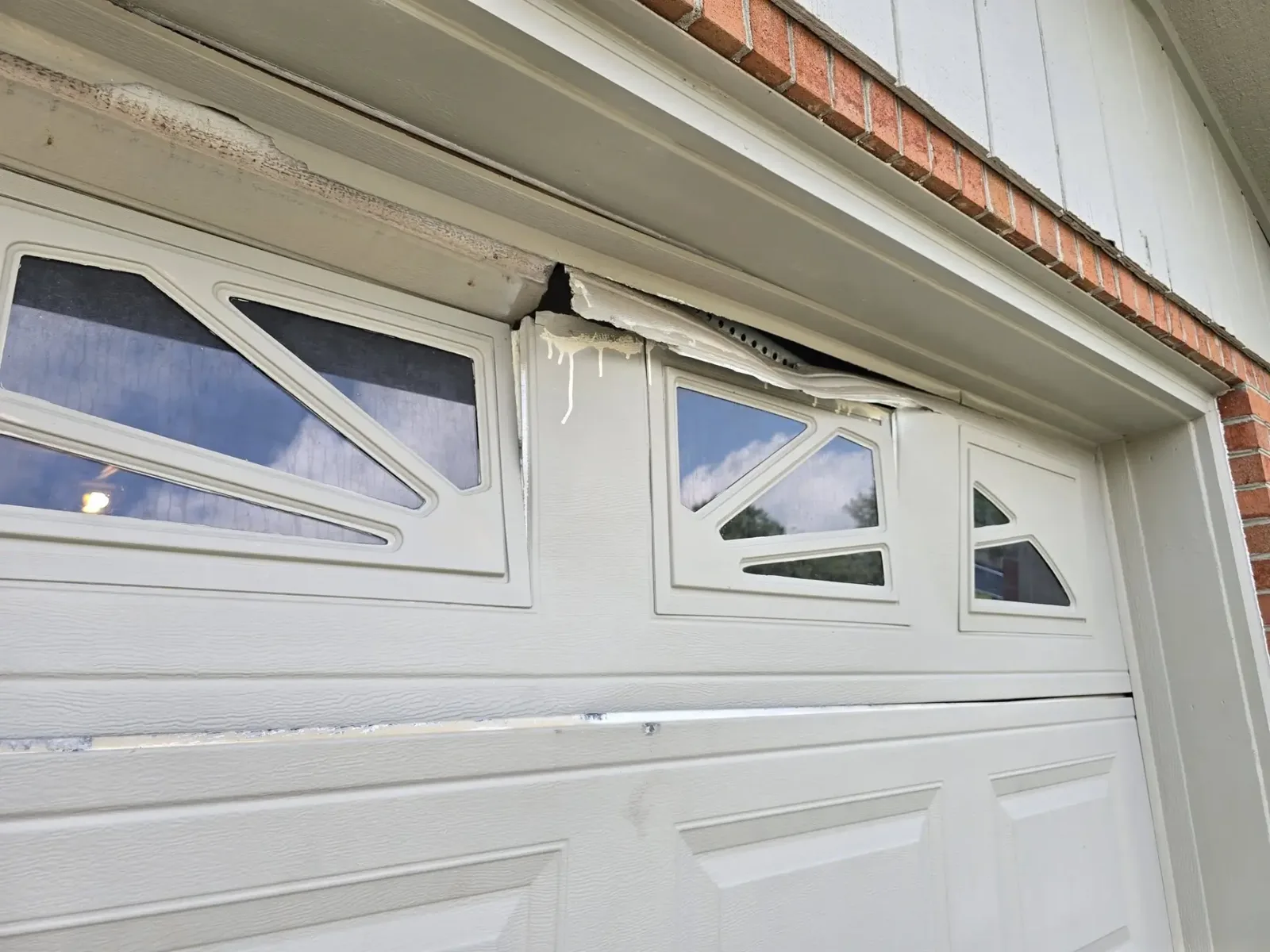 Damaged beige garage door with a hole and bent panel
