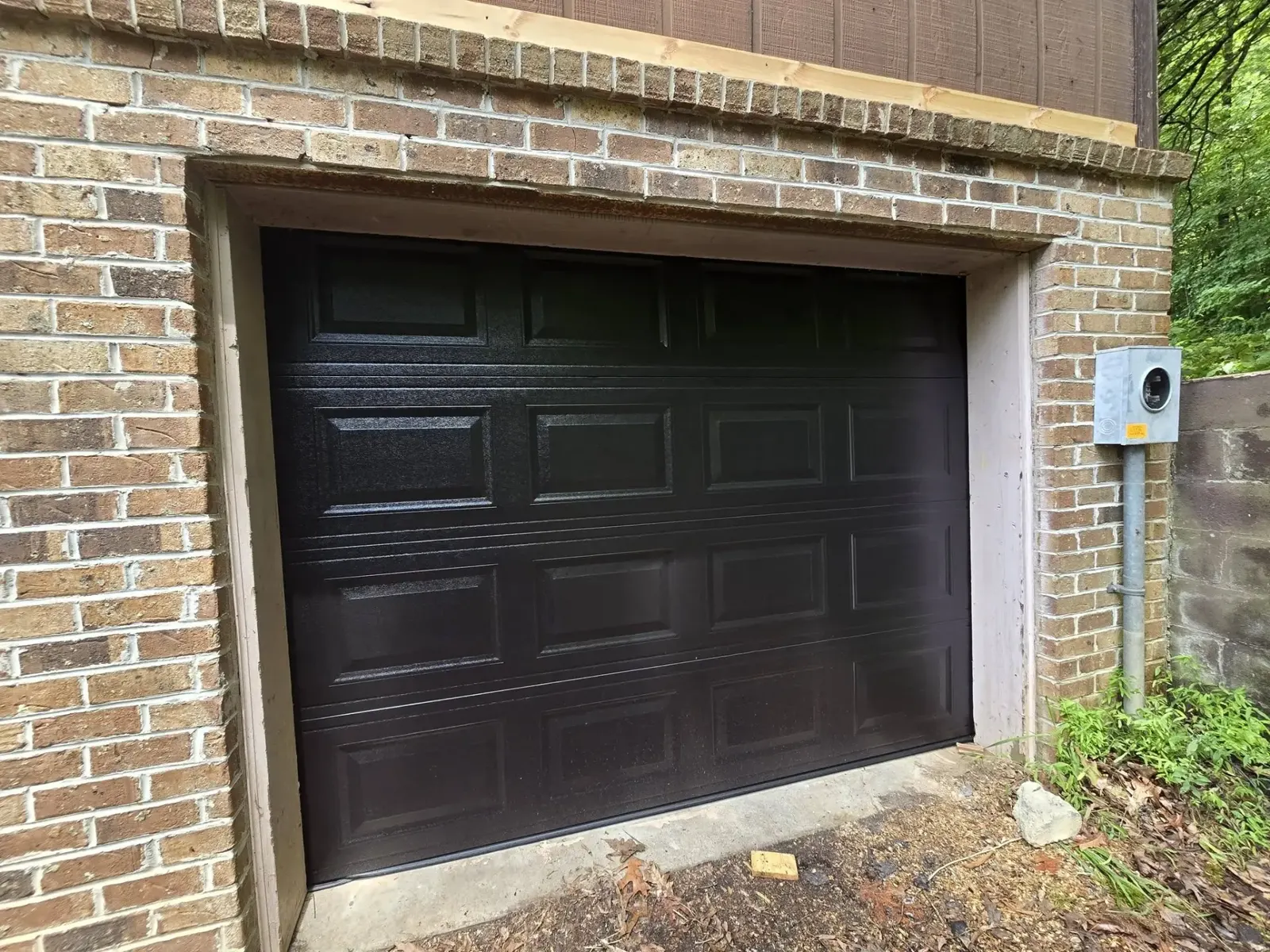 New black raised-panel garage door installed on a brick home