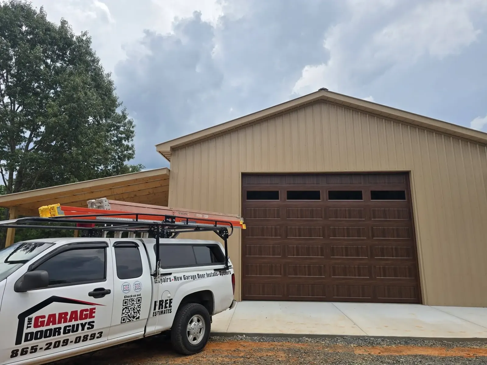 The Garage Door Guys truck at a new pole barn with a wood-look garage door
