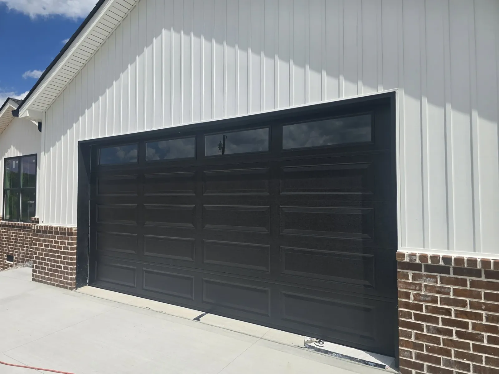 Black long-panel garage door with windows on a white board-and-batten home with brick accents